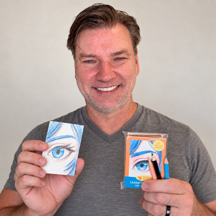 Michael, the creator of DoodleGoat, holding a completed anime eye drawing in one hand and the kit with three colored pencils in the other